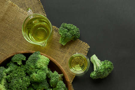 Fresh Broccoli in wooden bowl and seed oil in rustic style. Close up on a black background. copy space for text. Top view, flat lay.の写真素材