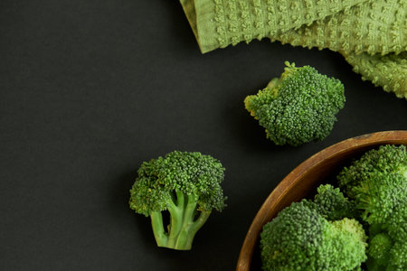 Fresh Broccoli in wooden bowl and seed oil in rustic style. Close up on a black background. copy...