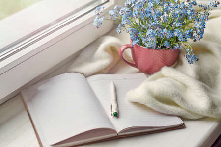 white warm plaid blanket and notebook, glasses on wooden rustic bench. Photo toned, selective focus. Cozy home still life: spring flowers with warm plaid on windowsillの写真素材