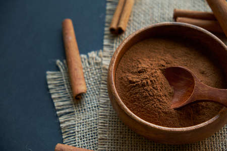 cinnamon sticks, tied with jute rope in rustic style. Ground cinnamon in a wooden bowl and vintage scoop. Close up on a black background. copy space for text. Top view, flat lay.の写真素材