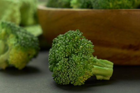 Fresh Broccoli in wooden bowl and seed oil in rustic style. Close up on a black background. side...