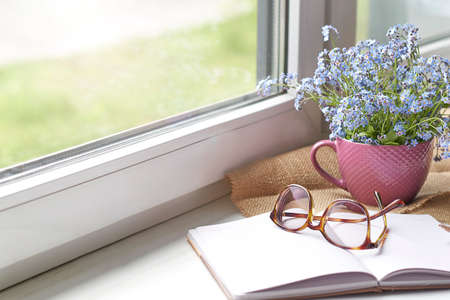 notebook and glasses, spring flowers on wooden rustic windowsill. Photo toned, selective focus. Cozy home still life: spring flowersの写真素材