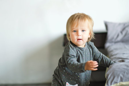 Portrait of very sweet little child. 1 year old baby stands next to the bed.