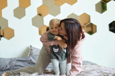 Happy family mother and baby playing, hugging and laughing in bedの写真素材