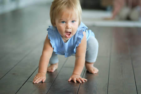 childhood, babyhood and people concept. happy little baby girl sitting on a wooden floor at home.