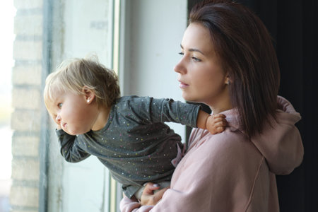 Closeup photo of mother holding baby boy while he is looking outside through window