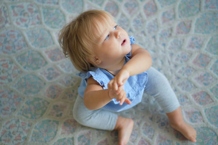 childhood, babyhood and people concept. happy little baby girl sitting on carpet at home. view from...