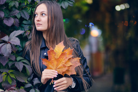 young beautiful woman in a stylish black leather jacket on a background of wild grapes. Autumn...