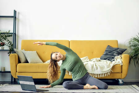 Beautiful young woman doing yoga at home. Fitness training online.の写真素材