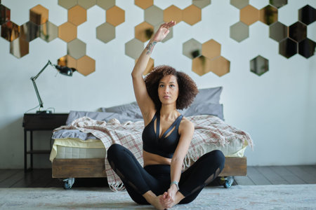 Attractive Afro American girl in sportswear is doing yoga and smiling