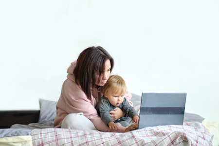 mom working remotely on laptop while taking care of her baby. Young mother on maternity leave trying...