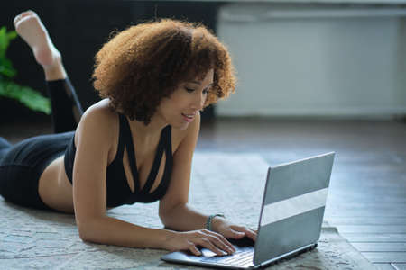 Smiling woman lying on the floor with her notebookの写真素材