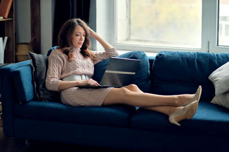 Young woman lying on a sofa and using a laptopの写真素材