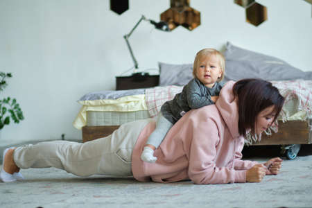 young mom does the plank when her daughter sits on her backの写真素材