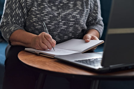 elderly lady writes with a pen in a diary, studies information on the Internet. Senior woman using...