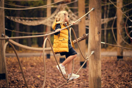 beautiful little girl climbs the rope park. sportswear modern brave girl. autumn fashionの写真素材