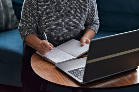 elderly lady writes with a pen in a diary, studies information on the Internet. Senior woman using...