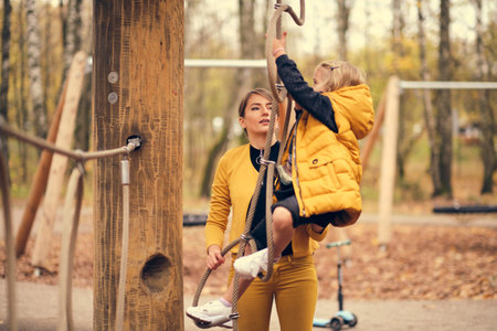 beautiful little girl climbs the rope park. sportswear modern brave girl. mom and daughter have fun...