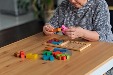 Activity can improve brain function. Elderly woman sitting at table and sorting jigsaw puzzle pieces, free space gameの写真素材