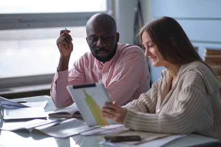 young African-American man with female colleague while working in cubicle at office. Ethnic...