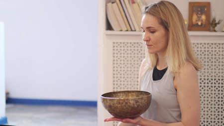 Woman playing on Tibetan singing bowl while sitting on yoga mat. Vintage tonned.の写真素材