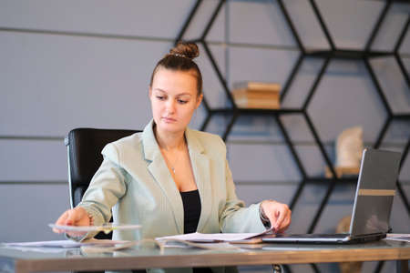 Busy female office worker. serious young female employee works in the office on her laptop. effective employee.の写真素材