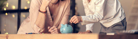 Mother and child putting coin into piggy bank. Education of children in financial literacy. Money, cash, investment.の写真素材