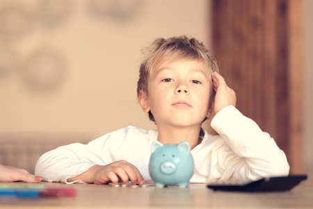childhood, money, investment and happy people concept smiling little boy with piggy bank and money at homeの写真素材