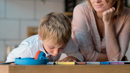 mom helping young son with laptop to do homework. Young woman teaching little boy to use the...