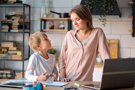 Young mother with toddler child working on the computer from home. multi tasking, freelance and motherhood concept working at home as her cute little boy plays on a tabletの写真素材
