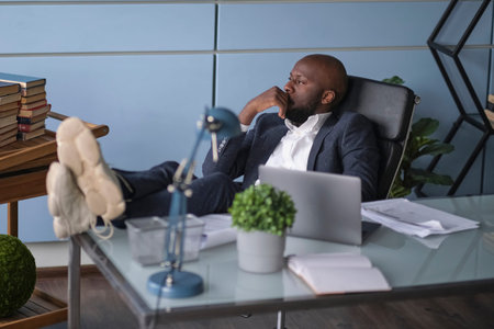 Relaxed worker finished work completed task taking break after hard workday putting head on hand. Thoughtful African American businessman looking out window sitting at office desk.の写真素材
