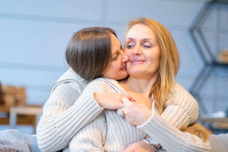 Beautiful family of mother and daughter together, hugging and kissing at home. senior mom and her adult daughter are hugging, looking at camera and smilingの写真素材