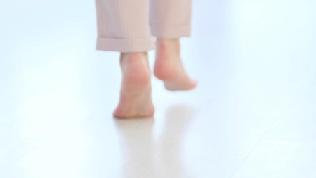 defocus, Side close up view of unrecognizable woman feet legs, barefoot girl standing indoors inside of modern home enjoy warm wooden heated floor. soft focusの写真素材