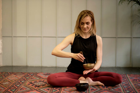 Woman playing on Tibetan singing bowl while sitting on yoga mat. Vintage tonned.の写真素材