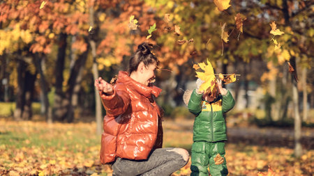 Mom and son throw autumn leaves in autumn park, family fun. family enjoying a walk in nature. happy motherhood concept.の写真素材