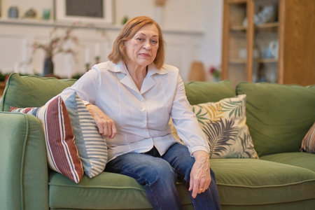 Portrait of an elderly woman sitting on a couch at old age home. Caucasian woman sitting on a sofa and looking at camera. Care for lonely pensioners.の写真素材