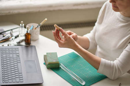 woman jeweler conducts online lesson in front of laptop. the teacher is taking online classes or watching a video tutorial on creating jewelryの写真素材