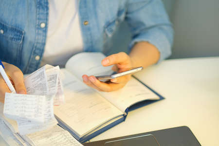 woman using a pen writing on bank account book while holding the bills to calculate in living room at home. Expenses, account, taxes, home budget concept.の写真素材
