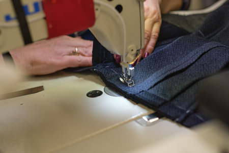 Female hands stitching white fabric on professional manufacturing machine at workplace. Close up...