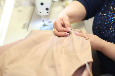 Talented female seamstress working with textile for sewing clothes. Close up view of sewing process. Light blurred backgroundの写真素材