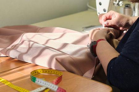 Talented female seamstress working with textile for sewing clothes. Close up view of sewing process. Light blurred backgroundの写真素材