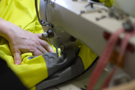 Female hands stitching white fabric on professional manufacturing machine at workplace. Close up...