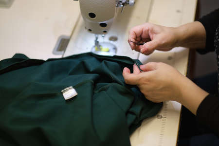 Female hands stitching white fabric on professional manufacturing machine at workplace. Close up view of sewing process. Light blurred backgroundの写真素材