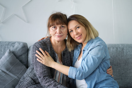 Head shot of beautiful adult daughter hug older mother at home, happy female two age generation...