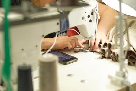 Female hands stitching white fabric on professional manufacturing machine at workplace. Close up...
