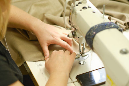 Female hands stitching white fabric on professional manufacturing machine at workplace. Close up...