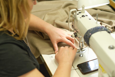 Female hands stitching white fabric on professional manufacturing machine at workplace. Close up...