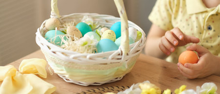 child boy wearing bunny ears sitting in the kitchen at the table. child holding painted eggs preparing for easter.の写真素材