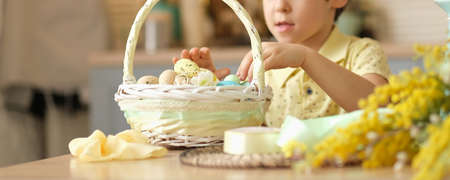 child boy wearing bunny ears sitting in the kitchen at the table. child holding painted eggs preparing for easter.の写真素材