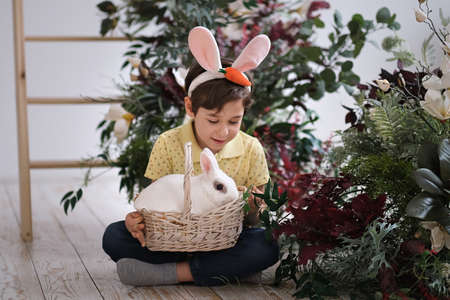 Happy easter. Child boy in bunny ears and hare sits in a wicker basket for spring holiday celebration. soft focusの写真素材